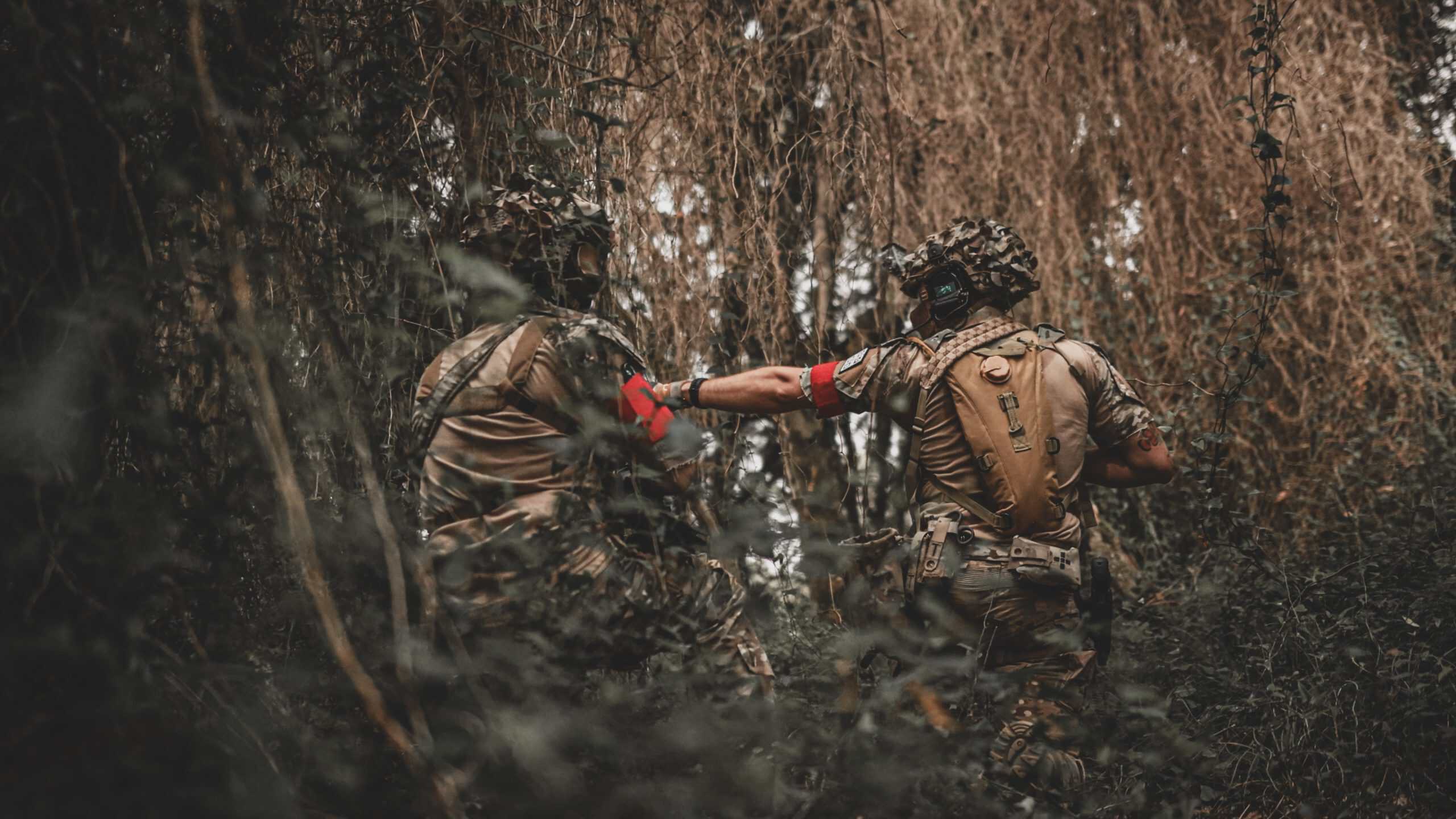 Dos jugadores de airsoft en bosque cerrado pasándose una granada de humo