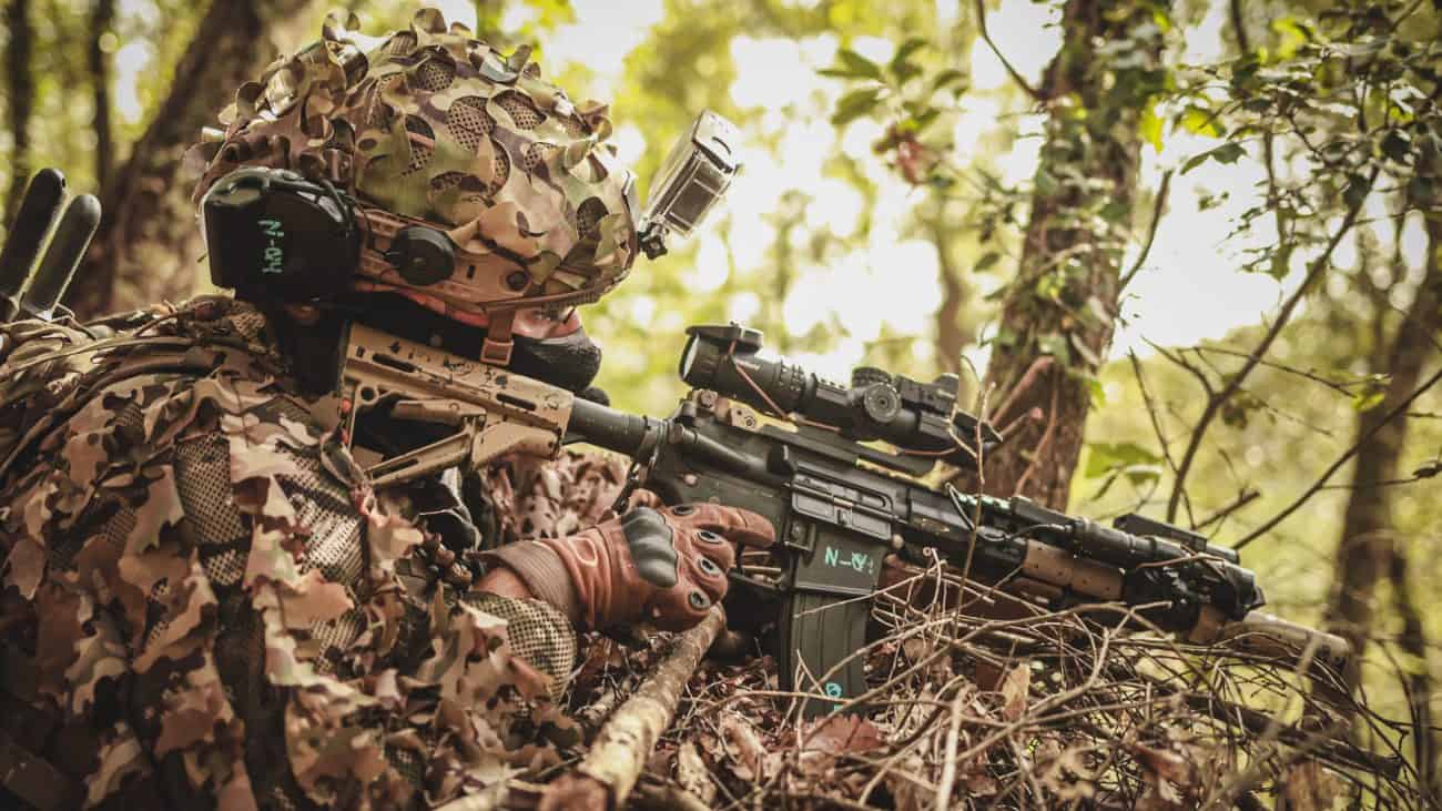 Jugador de airsoft camuflado con ghillie apuntando con una réplica M4 en el bosque