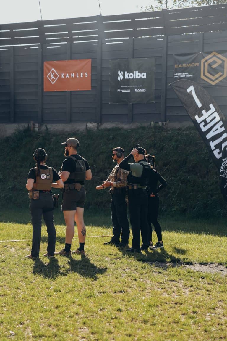 Grupo de atletas con chaleco portaplacas y protección auditiva en la línea de tiro