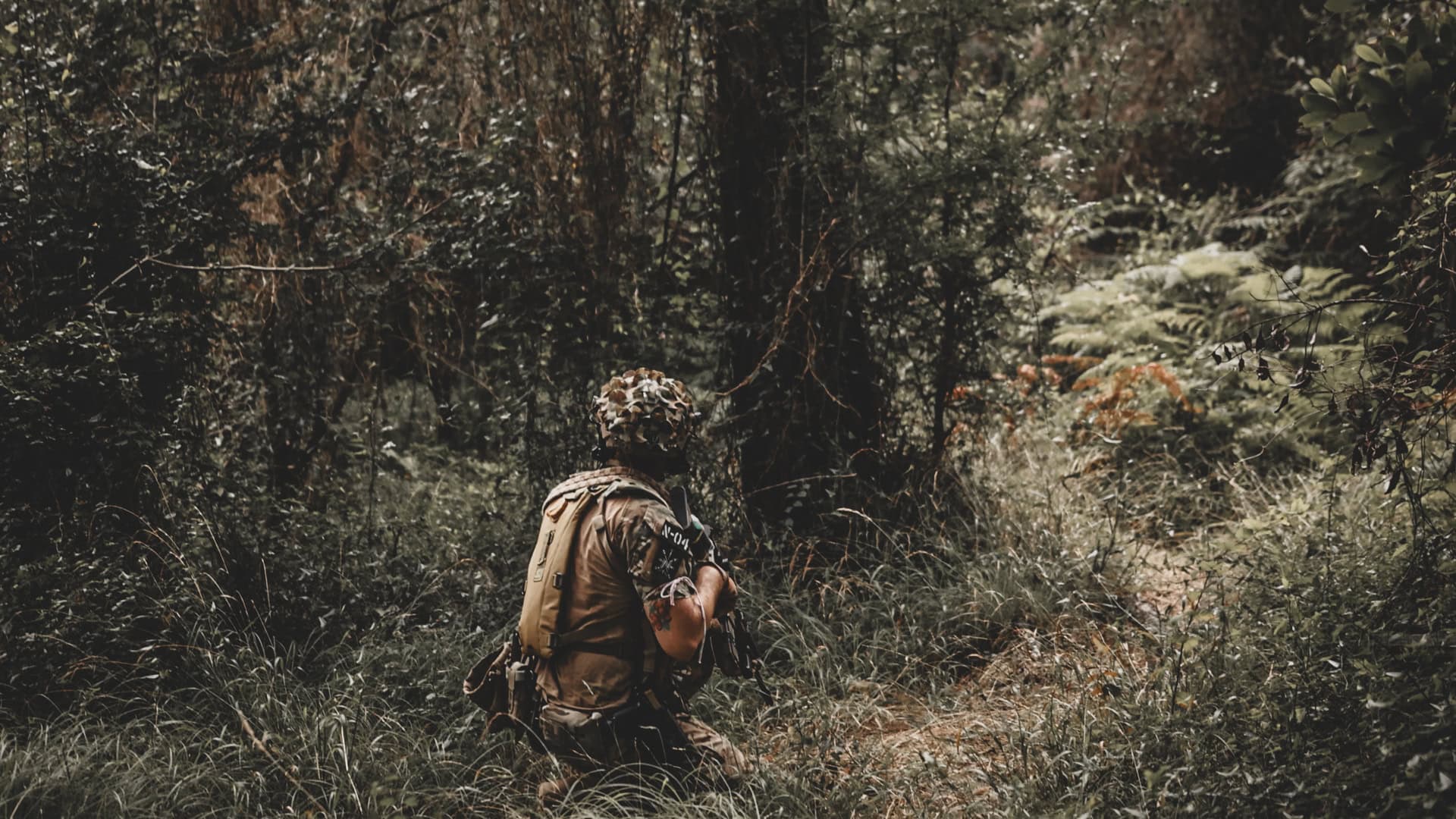 Jugador de airsoft arrodillado entre helechos en un bosque