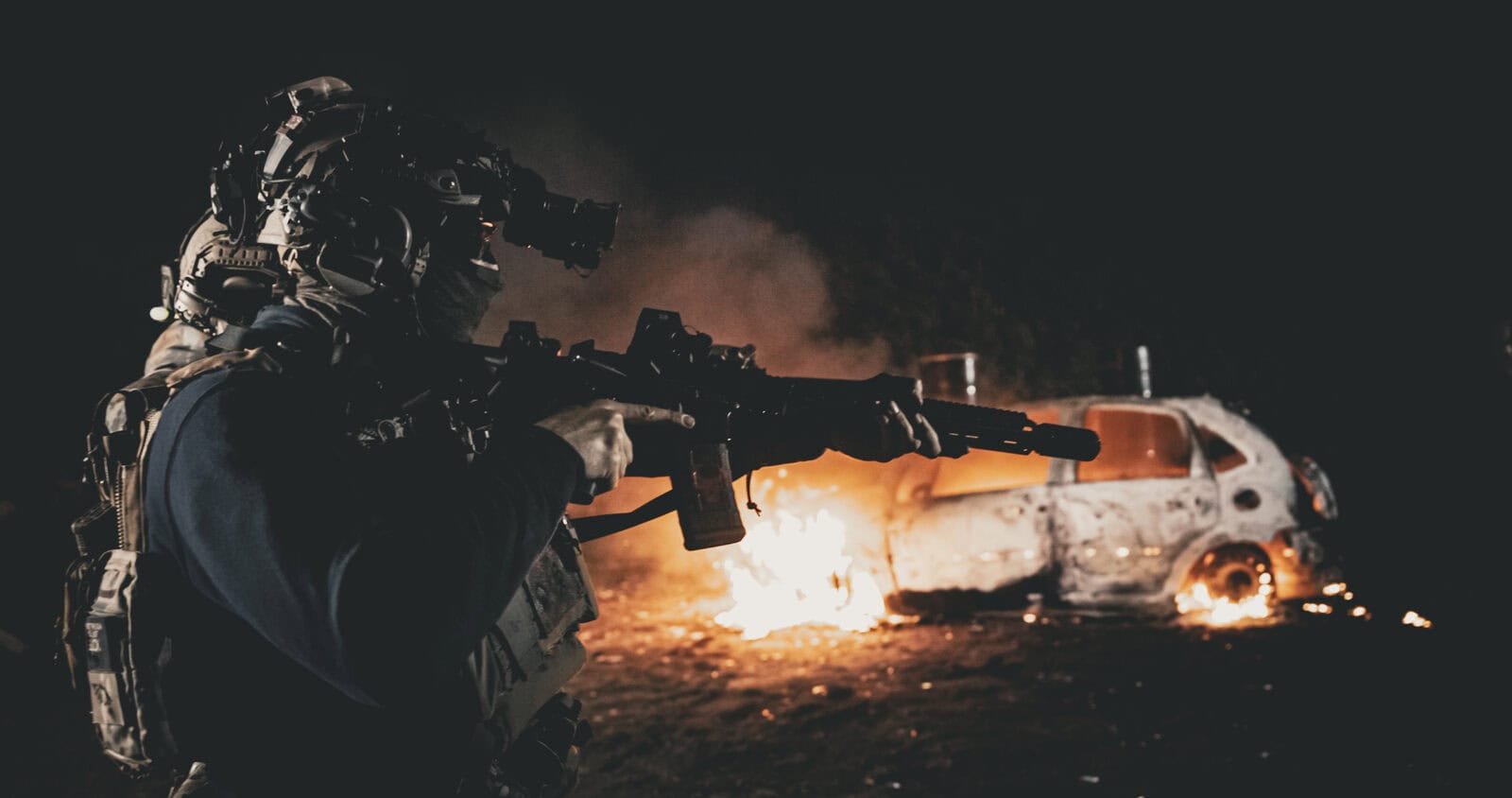 Jugador apuntando con su réplica junto a un coche ardiendo, con ropa Brothers in Arms