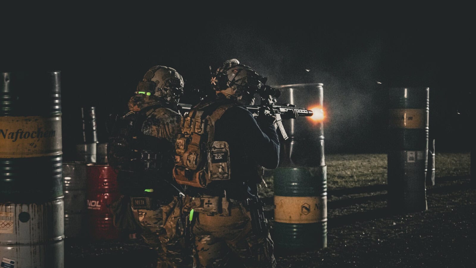Dos operadores con equipo Brothers in Arms entre bidones durante un ejercicio nocturno